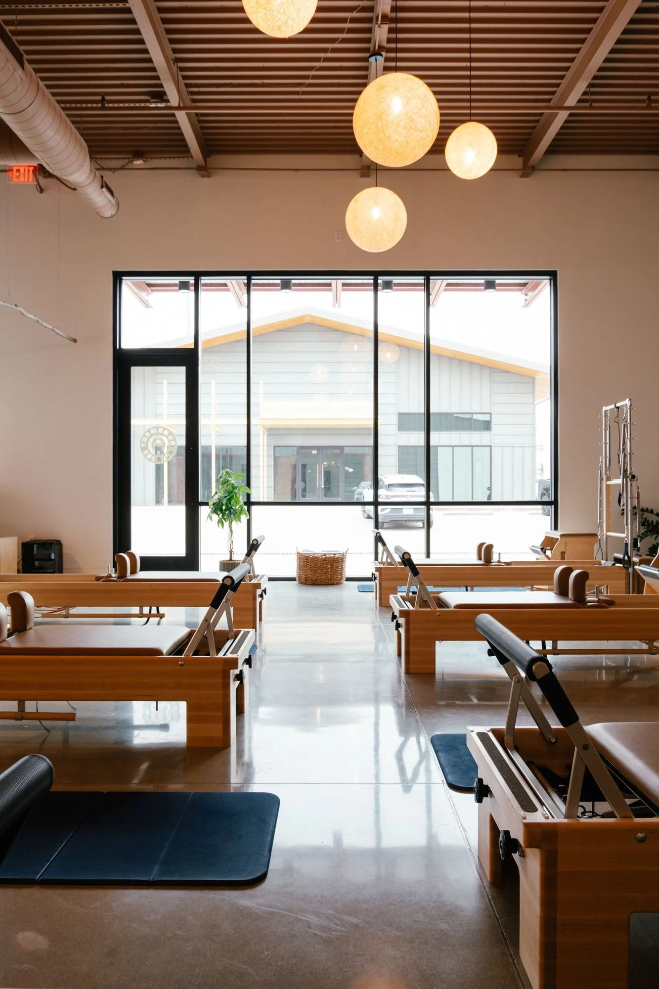 Interior of Monument Pilates studio with wooden reformer machines and hanging globe lights